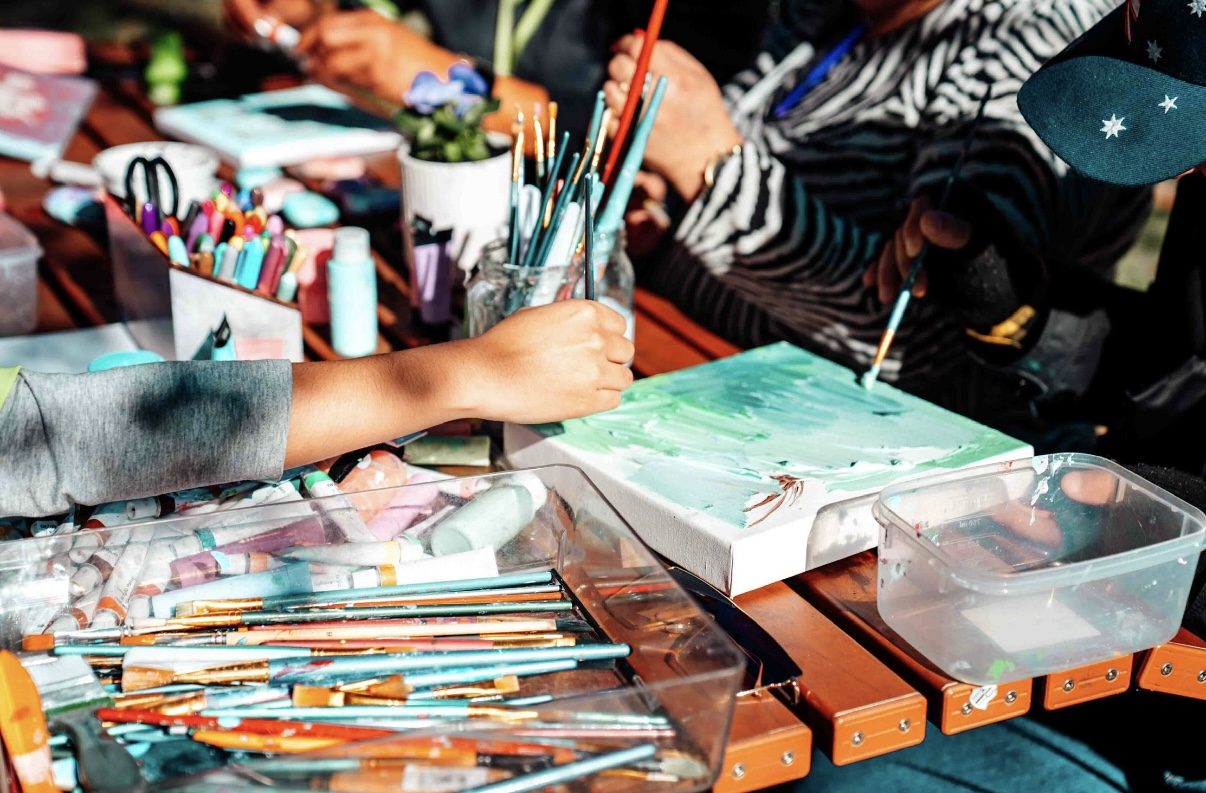 Participants and support workers painting together at an outdoor art session.