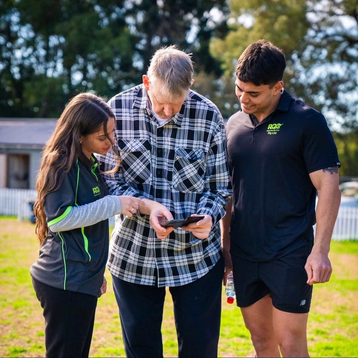 Two Right Quality Care support workers helping a client with his phone outdoors.